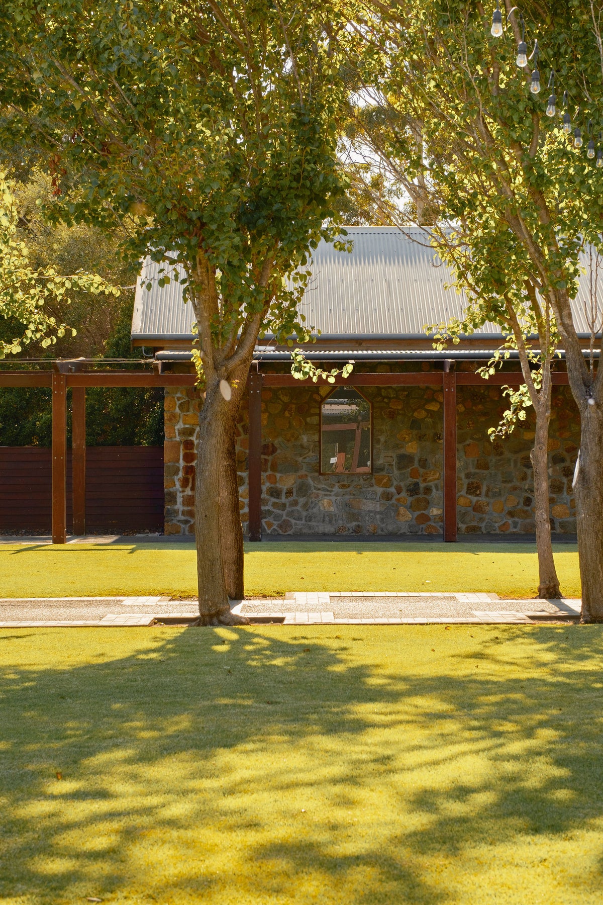 Stone cellar door building with a corrugated roof, shaded by trees on a lawn
