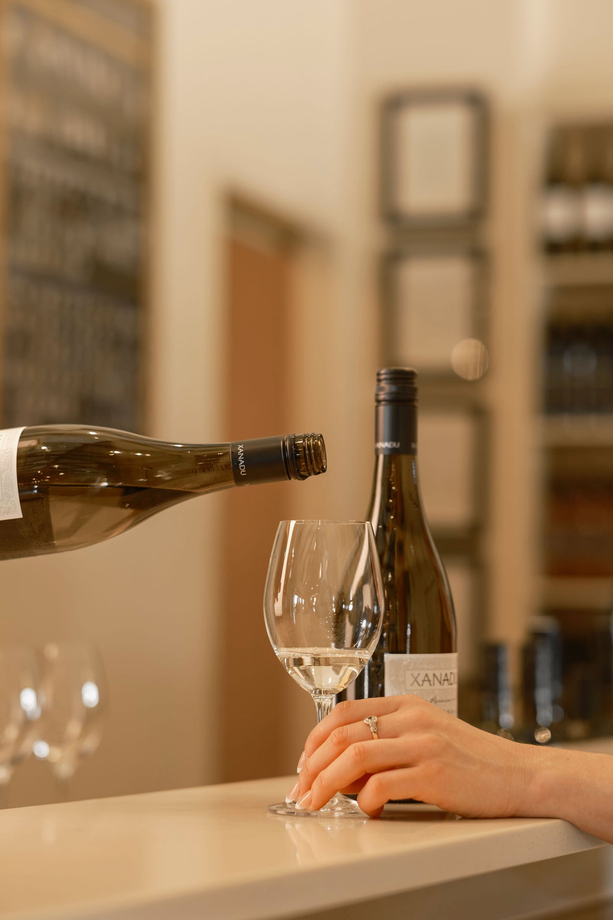 Hand pouring a bottle of Xanadu wine into a glass at the cellar door tasting counter