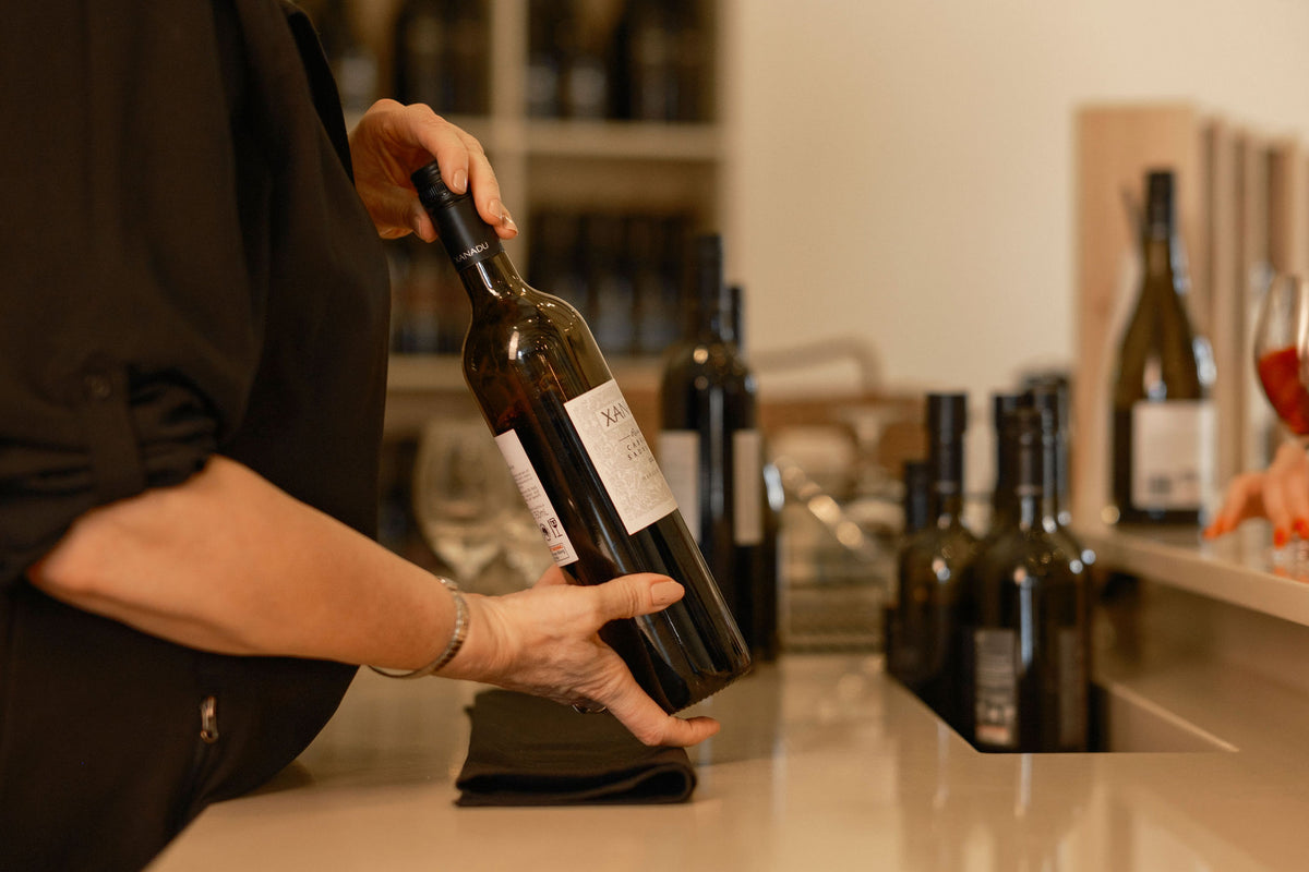Cellar door staff member holding a bottle of Xanadu Cabernet Sauvignon at the tasting counter