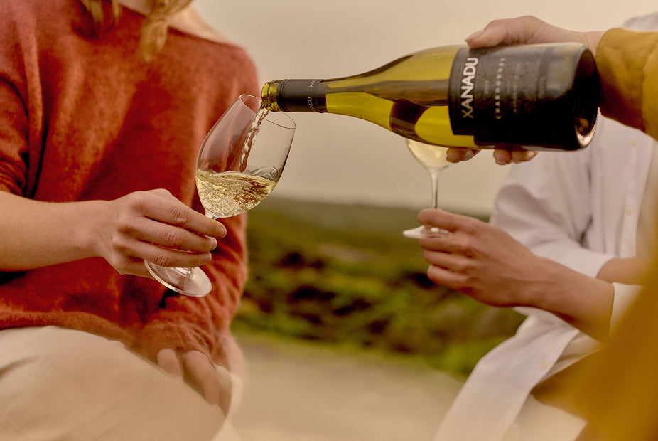 Two people toasting with glasses of Xanadu Chardonnay outdoors