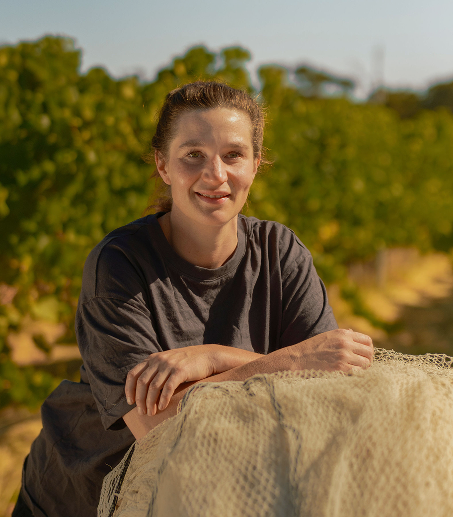 Portrait of a smiling Xanadu vineyard team member resting on a bundle of netting among the vines