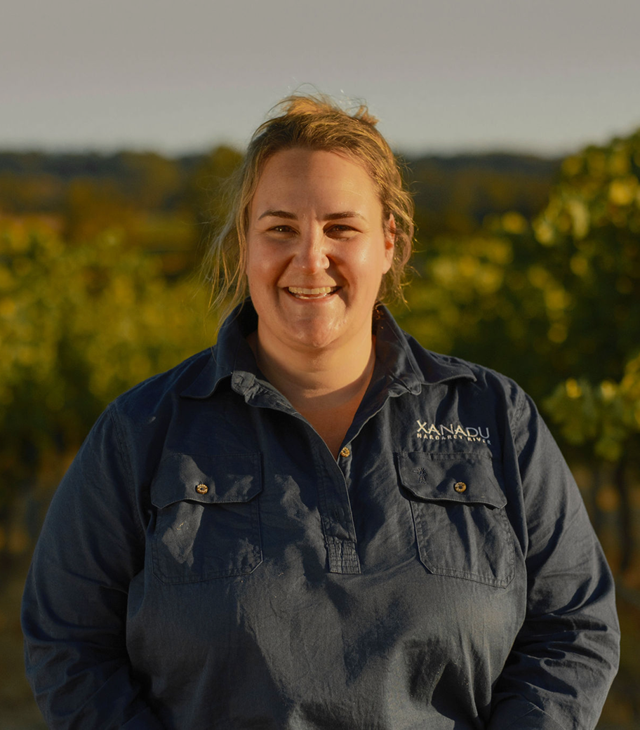 Portrait of a smiling Xanadu vineyard team member in branded work shirt standing among the vines at sunset
