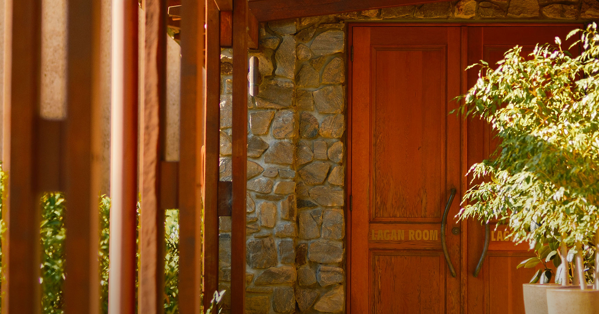 Timber pergola walkway leading to the Lagan Room's stone entrance with wooden doors and a potted plant