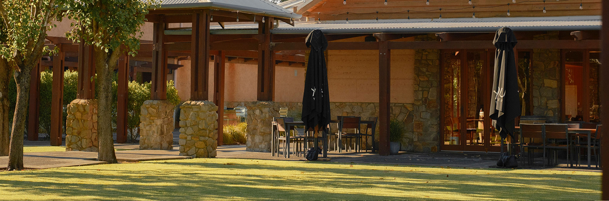 Outdoor dining terrace with closed umbrellas and seating along the stone and timber winery building