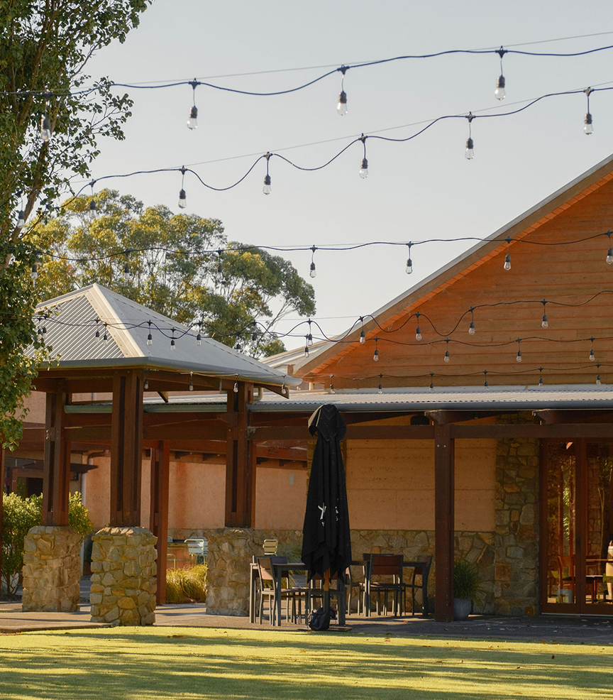 String lights strung above an outdoor courtyard beside the timber-clad winery building