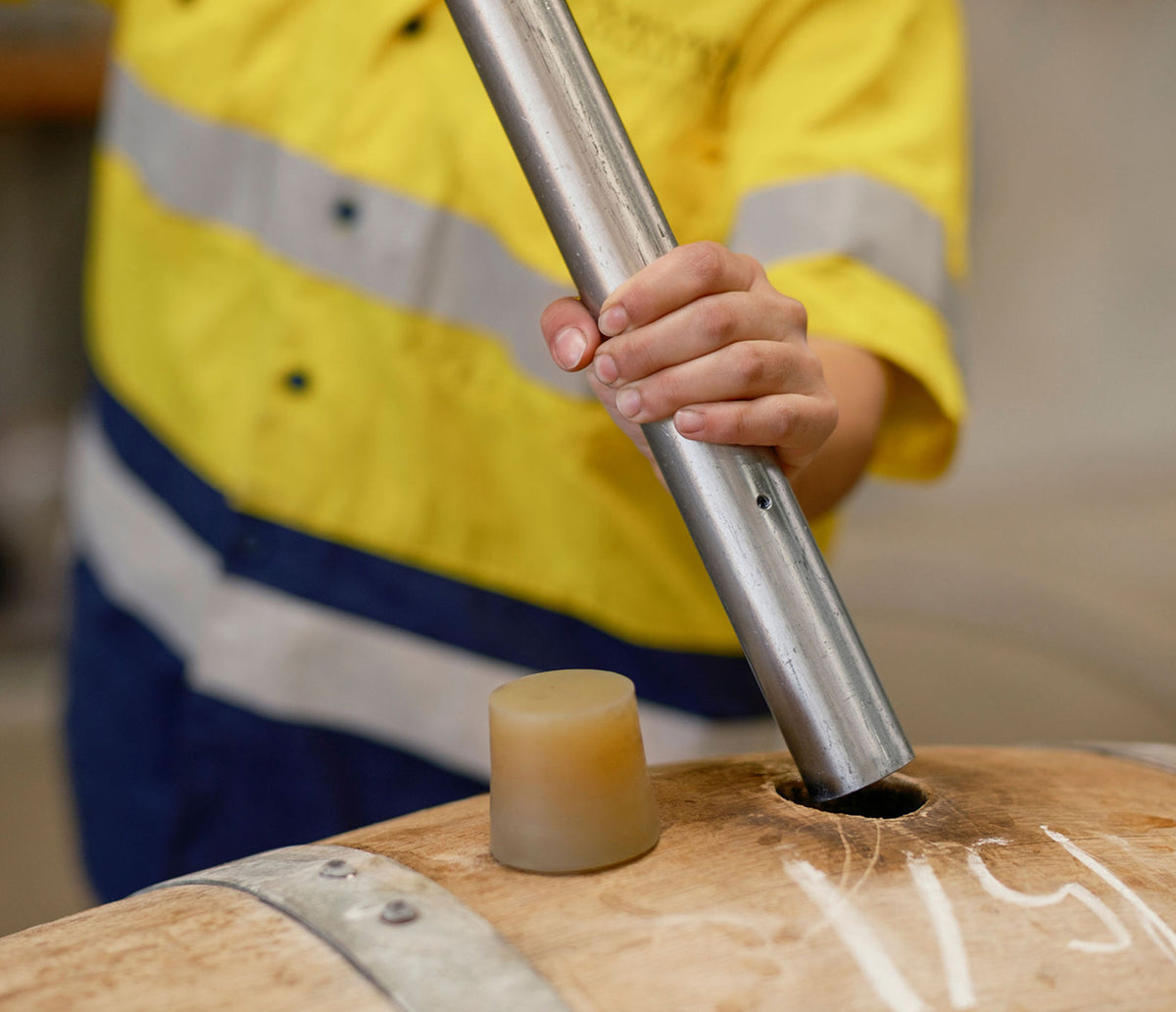 Winery worker in high-visibility jacket inserting a bung into a wine barrel