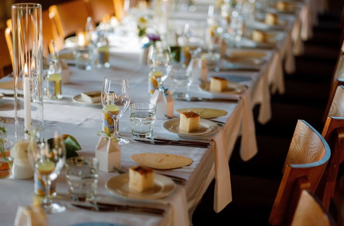 Long banquet table set for a wedding or function with candles, wine glasses, and dessert plates