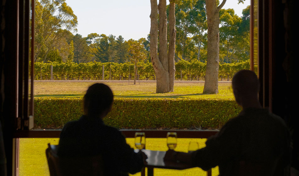 Silhouetted guests seated at a table overlooking vineyard rows through open restaurant doors at Xanadu