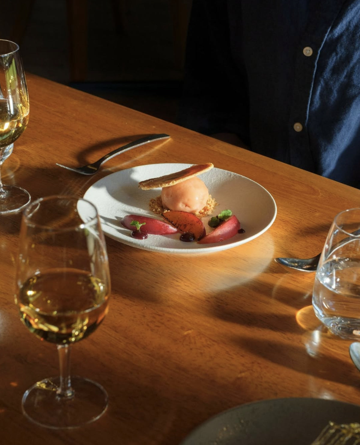 Dessert plate with ice cream, poached fruit and a tuile beside glasses of white wine at the Xanadu restaurant